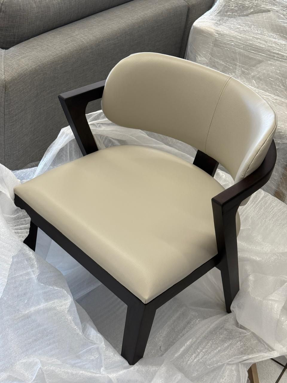 Beige leather dining chair with dark brown frame and legs. Curved back dining chair.