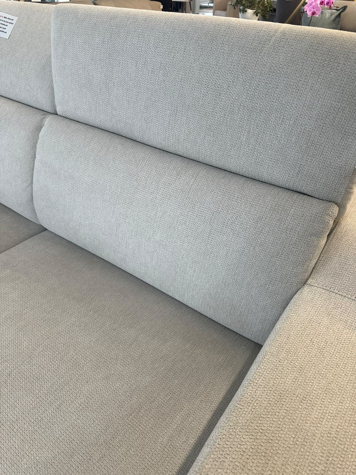 Close-up of a light gray textured fabric sofa cushion and armrest in a furniture showroom.